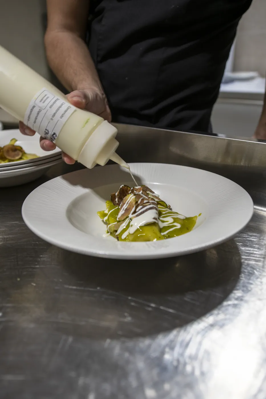 La mano dello chef che rifinisce il piatto con la crema