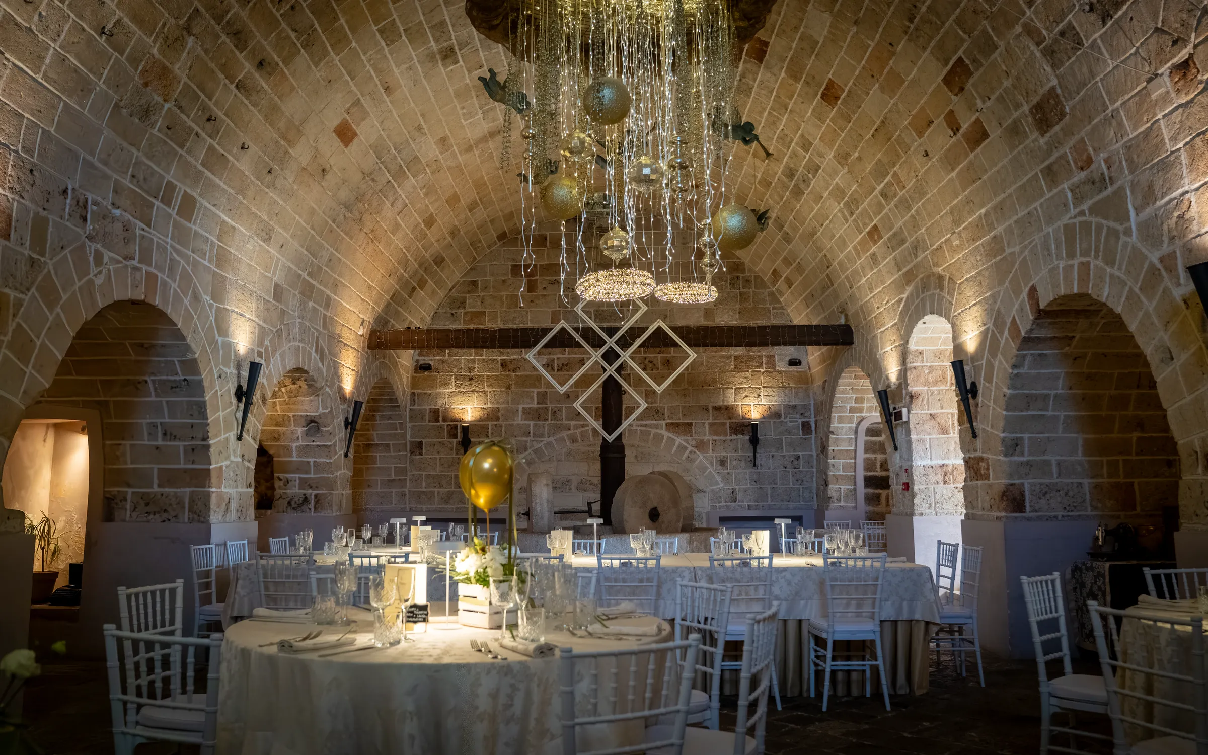 La sala ipogea con i tavoli rotondi apparecchiati, l'antica macina e il lampadario di luci